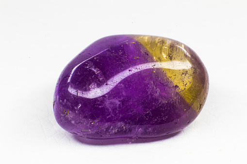 Real tumbled Ametrine stone macro isolated on white surface. Purple crystal with a bit of yellow coloration on the end.