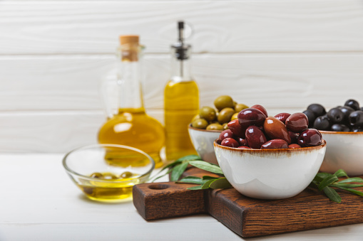 Green and black olives on a textured background. Different types of olives in bowls and olive oil with fresh olive leaves. Delicacy.Mediterranean Kitchen. Copy space.