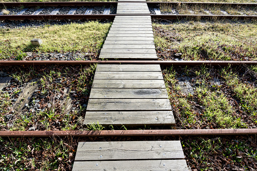walkway over rusty rails with wooden sleepers and encroaching vegetation