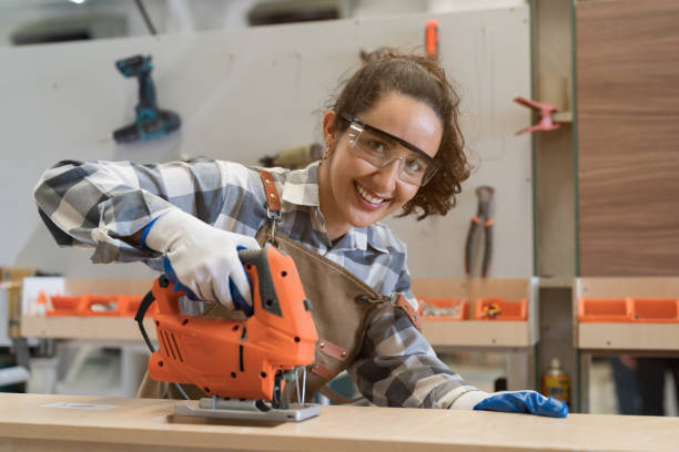 istock Female carpenter using electric hand jigsaws in carpentry workshop. Joiner female working in wood factory 1718865494
