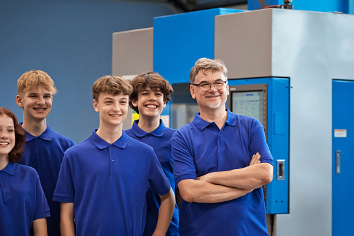 Teacher and group of students posing together at workshop. Standing together in front of CNC machine.