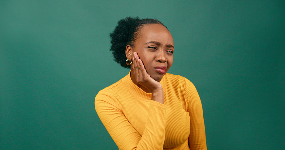 Young Black woman rubs jaw in pain, toothache, studio green background orange. High quality photo