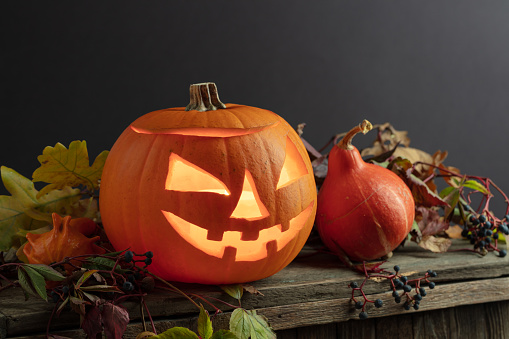 Halloween pumpkin head jack lantern with dried-up leaves. Halloween holidays art design, celebration. Carved Halloween pumpkin with burning candle.