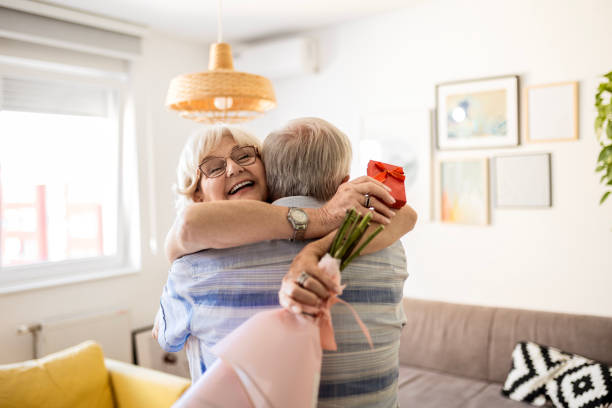 Senior Woman's Gift at Home Smiling senior woman receives present box and kissing her husband at home senior birthday card stock pictures, royalty-free photos & images