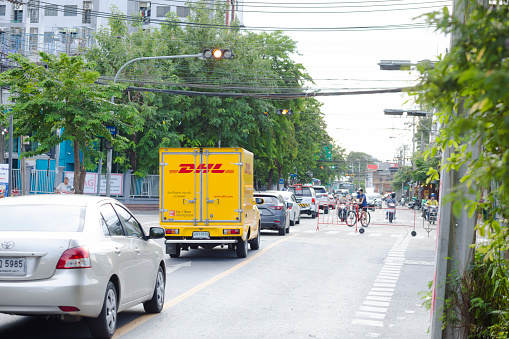 German parcel DHL semi-truck in queued traffic in Bangkok in street Ladprao71 area in district Ladprao. Scene ie sclose to an intersection. In background is a cyclist in traffic