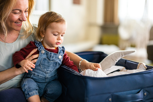 Happy mother and her small daughter put clothes in a suitcase for the trip at home