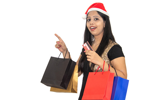 Amazed woman in Santa hat holding shopping bags and credit card showing advertisement recommending Christmas discount offer