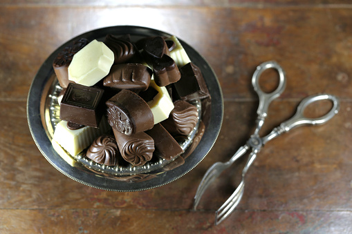 Belgian chocolate pralines in a silver bowl on rustic wooden background