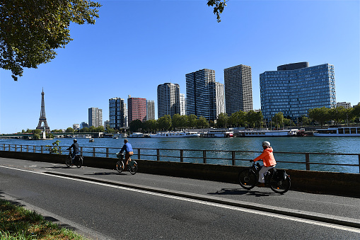 Paris, France-09 24 2023: People riding bicycles on the banks of the Seine river with the Eiffel tower and the Beaugrenelle skyscrapers in the background, France.