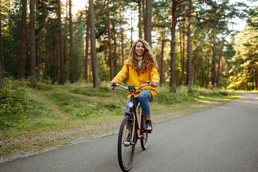 Smiling woman on a bicycle in an autumn park. Beautiful female tourist rides a bicycle, enjoys the sunny warm weather. Lifestyle, weekend concept.