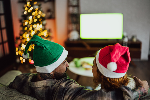 Rear view of a couple watching television and talking about Christmas time at home - Green screen mock up