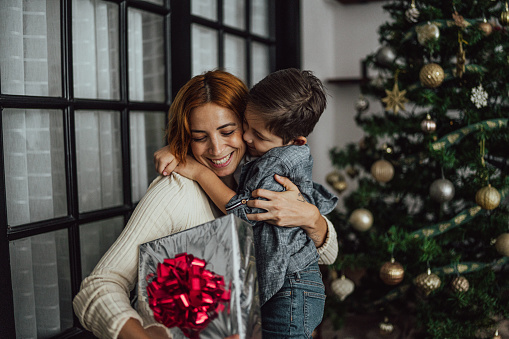 Mother giving Christmas gifts to son at the home