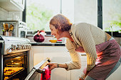 Mid adult woman opening oven to check cookies in kitchen at home