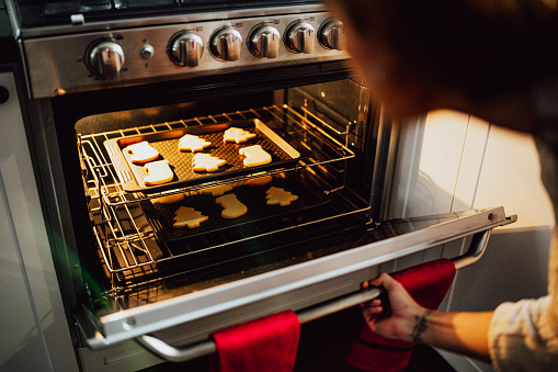 Woman opening oven to check cookies in kitchen at the home
