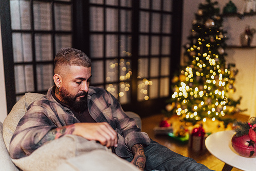 Sad mature man sitting on the sofa alone on Christmas Day at home