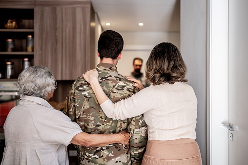 Rear view of an army soldier arm around with his grandmother and mother at home