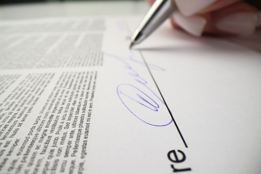 Woman signs contract papers with pen showing agreement with rules. Female person puts personal signature above line on paper sheet