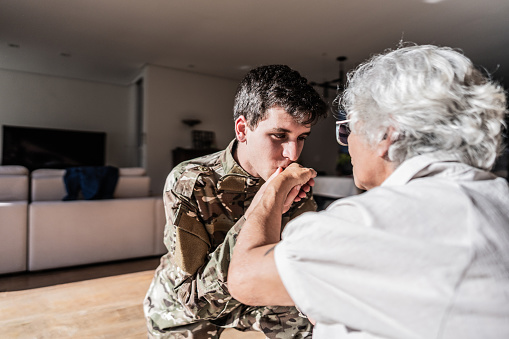 Army soldier kissing hand of his grandmother at home