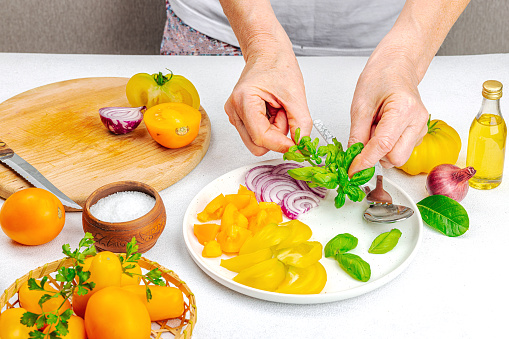 A woman is preparing a tomato salad. Ripe vegetables, herbs, aromatic spices, olive oil. Home cooking, fresh ingredients