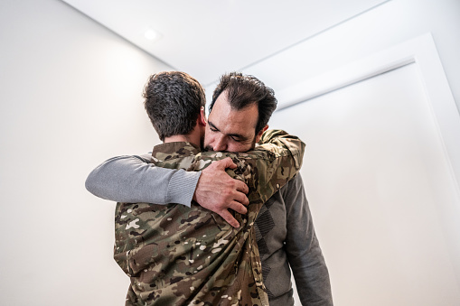 Mature man embracing to his soldier son at home