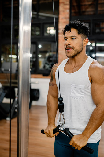 Muscular man using a pull-down machine to work on the muscles of the upper body during training session in gym