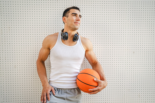 One young caucasian man male athlete stand outdoor hold basketball ball wear white tank top a-shirt strong muscular real person copy space happy smile confident healthy lifestyle concept