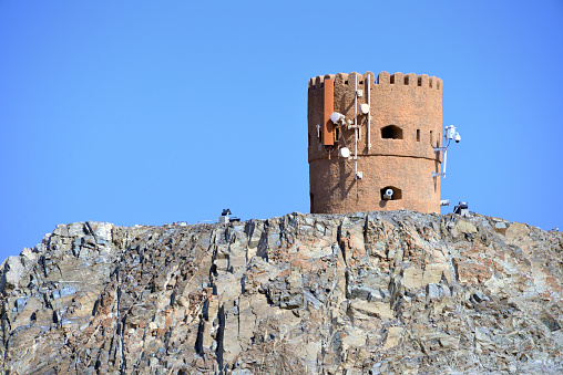 Riyam, Wilayat Muttrah, Muscat, Oman: old coastal defense tower at the harbor entrance, probably of Portuguese origin, still equipped with 17th century cannons aiming in the four directions, now covered in mobile phone network antennas - perched on a rocky hill just south of the Muscat marine tower - Al-Bahri road, the corniche.