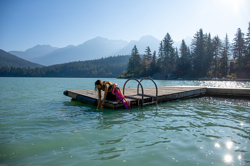 She reaches down and splashes her face with glacial water at Green Lake, in Whistler, BC