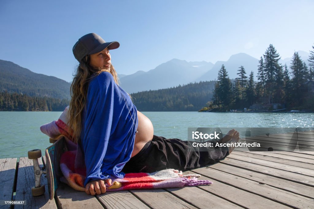 Young woman relaxes on lakeside dock in the morning With her pregnant belly exposed, she soaks up the sunshine. At Green Lake, in Whistler, BC. Discovery Stock Photo