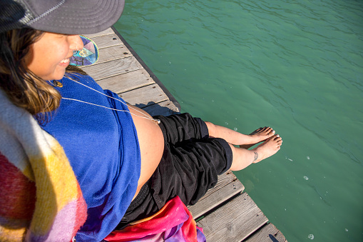 Pregnant woman relaxes on lakeside dock in the morning
