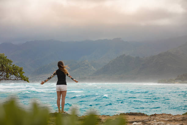 Young woman surrounded by ocean and mountains. Feeling free.