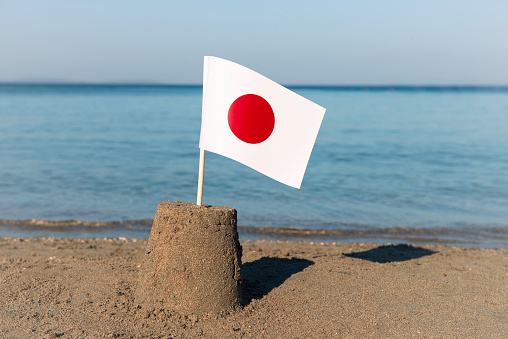A sandcastle on the beach with the flag of Japan on top.