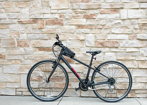 Matte black, hybrid bicycle set outdoors against a tan flagstone wall.