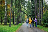 Mother and three teenagers walking in public park on a rainy autumn day.