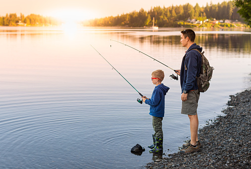 Father and son fishing by a lake at sunset.