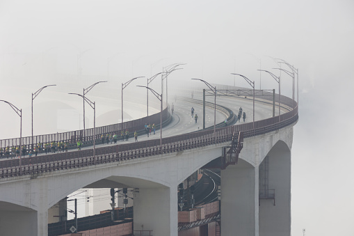 March 12, 2023 Lisbon, Portugal: Thick fog envelopes the bridge - people run a marathon on the bridge. Mid shot