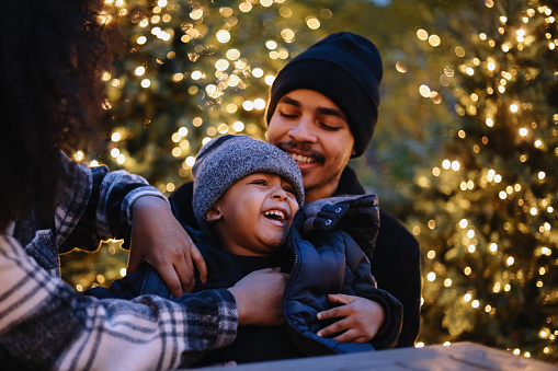 mom and dad playing with baby boy under decorated city lights in New York City.