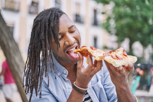 hombre caribeño con rastas comiendo una rebanada de pizza en la calle. concepto de comida rápida - beauty beautiful braids dairy product fotografías e imágenes de stock