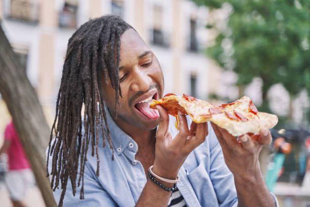 карибский мужчина с дредами ест кусочек пиццы на улице. концепция фаст-фуда - beauty beautiful braids dairy product стоковые фото и изображения