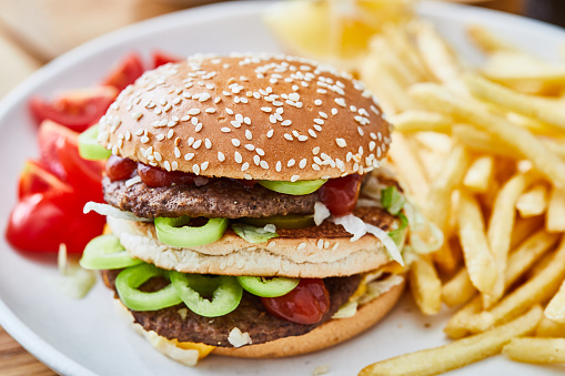 Fresh, colorful, tasty and delicious double beef cheese burger with French fries, tomato, onion, served  on a plate, bar, restaurant or home kitchen table, close up view with copy space, representing fast food and city life, indulgence and joy through gourmet lifestyle