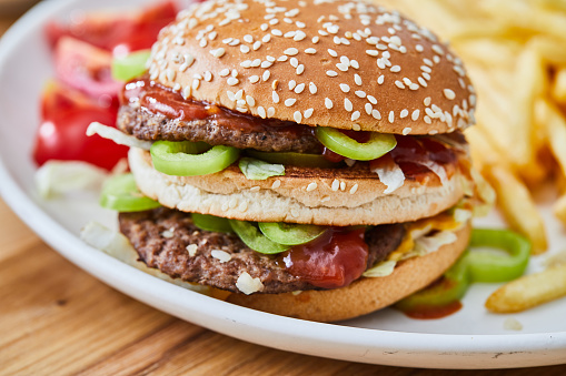 Fresh, colorful, tasty and delicious double beef cheese burger with French fries, tomato, onion, served  on a plate, bar, restaurant or home kitchen table, close up view with copy space, representing fast food and city life, indulgence and joy through gourmet lifestyle