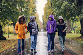 Mother and three teenagers enjoying rain in public park on an autumn day.