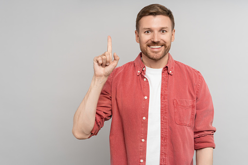 Look over there. Satisfied smiling man pointing up presenting product looking at camera. Handsome happy guy with idea gesture showing direction with finger isolated studio background. Copy free space