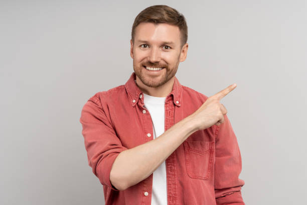 Pleased middle aged man smiling broadly points with index finger in right corner empty space for ad.