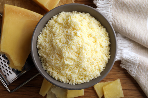 Delicious grated parmesan cheese in bowl on wooden table, flat lay