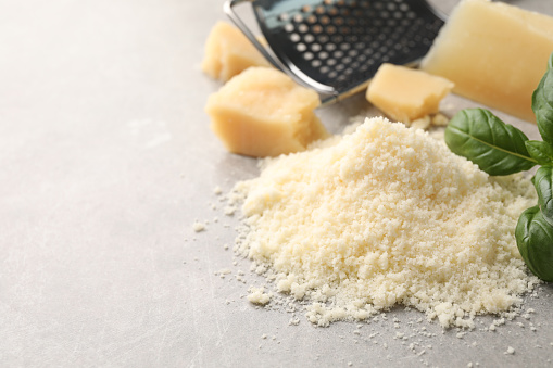 Pile of grated parmesan cheese on light table, closeup. Space for text