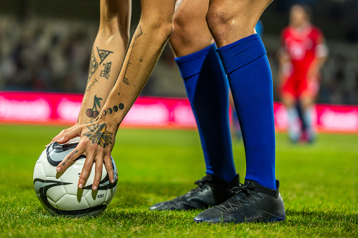 Woman football player holding ball and preparing for penalty kick, legs and tattooed hands medium shot