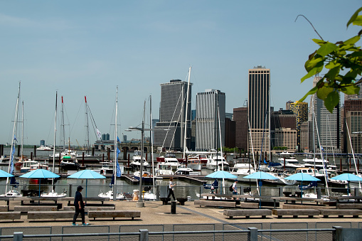 A picturesque scene in Brooklyn Heights, NY, USA, featuring a charming pier adorned with boats and elegant sailing yachts, set against a scenic waterfront backdrop.