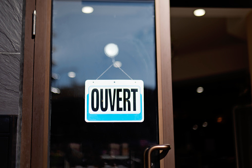 Storefront sign open in french « ouvert ». No people, blurred background, reflections on the window. Horizontal outdoors shot with copy space. This was taken in Montreal, Quebec, Canada.