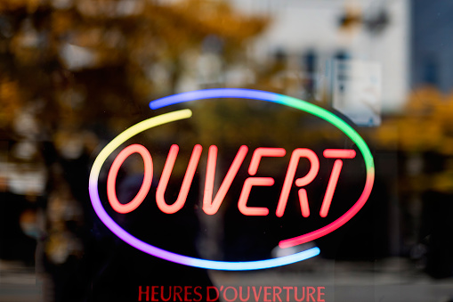 Storefront sign open in french « ouvert ». No people, blurred background, reflections on the window. Horizontal outdoors shot with copy space. This was taken in Montreal, Quebec, Canada.